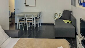 A hotel room with a bed, a grey sofa, a dining table with chairs, and a TV. - Sciacchetrà Ground Floor Apartment with AC (Monterosso al Mare)
