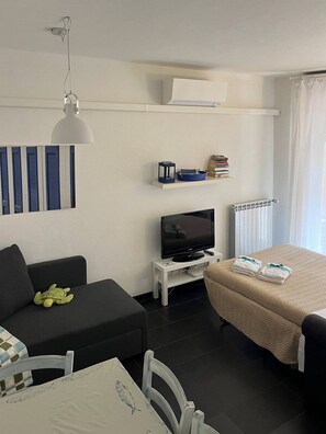 Une chambre d’hôtel moderne équipée d’un canapé, d’un téléviseur posé sur un meuble, d’une petite table avec une chaise et d’un lit avec des serviettes.