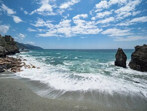 A beach with rocky outcrops and waves, under a partly cloudy sky.