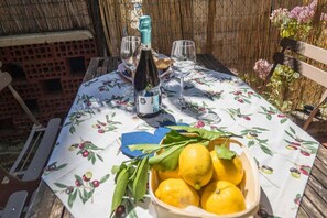 A table set outdoors with a bottle of wine, glasses, a bowl of lemons, and a floral tablecloth.