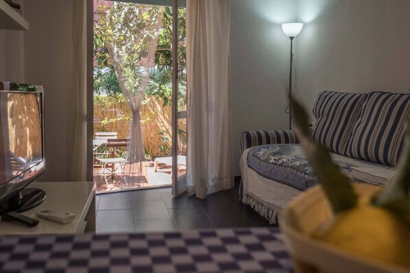 Ein Zimmer mit einer Couch, einer Lampe, einem Fernseher und Blick auf eine Außenveranda mit Tisch und Stühlen.