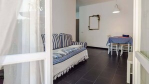A room with a sofa, a dining table with chairs, a hanging light fixture, and a wall-mounted mirror. - Sciacchetrà Ground Floor Apartment with AC (Monterosso al Mare)