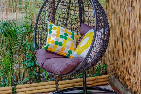 A hanging chair with cushions, surrounded by bamboo and greenery.