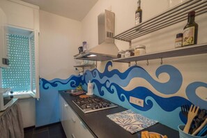 A kitchen with a stove, microwave, and a window with blinds. - Sciacchetrà Ground Floor Apartment with AC (Monterosso al Mare)