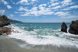 A coastal beach with rocky formations, waves, and a clear sky.
