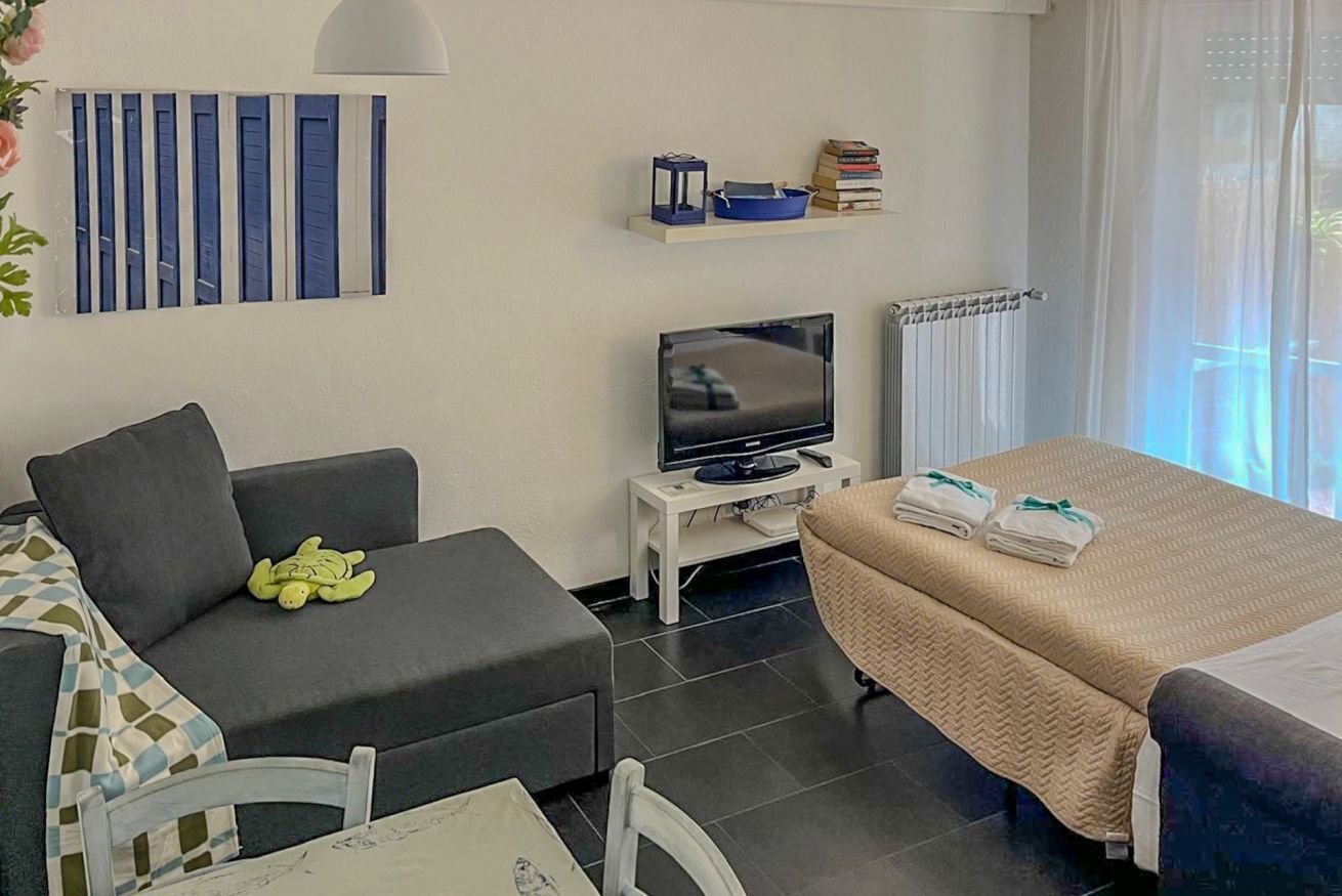 Ett modernt hotellrum med en soffa, en säng, en tv, ett litet bord och ett fönster med gardiner.