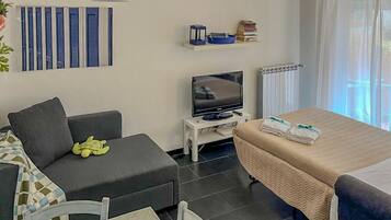 Ett modernt hotellrum med en soffa, en säng, en tv, ett litet bord och ett fönster med gardiner.