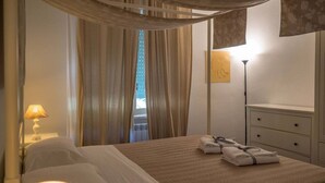 Een hotelkamer met een bed, nachtkastje met lamp, kapstok en raam met gordijnen.