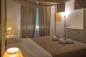 A hotel room with a bed, a nightstand with a lamp, a dresser, and a window with curtains.