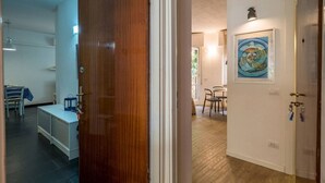 Een gang met een houten deur, een witte muur met een lijst en een eethoek met stoelen en een tafel.