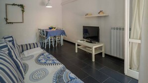 Een woonkamer met een bank, een televisie op een meubel, een eettafel met stoelen, en een radiator.