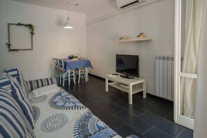 Un salon comprenant un canapé, un téléviseur posé sur un meuble, une table à manger avec des chaises et un radiateur.