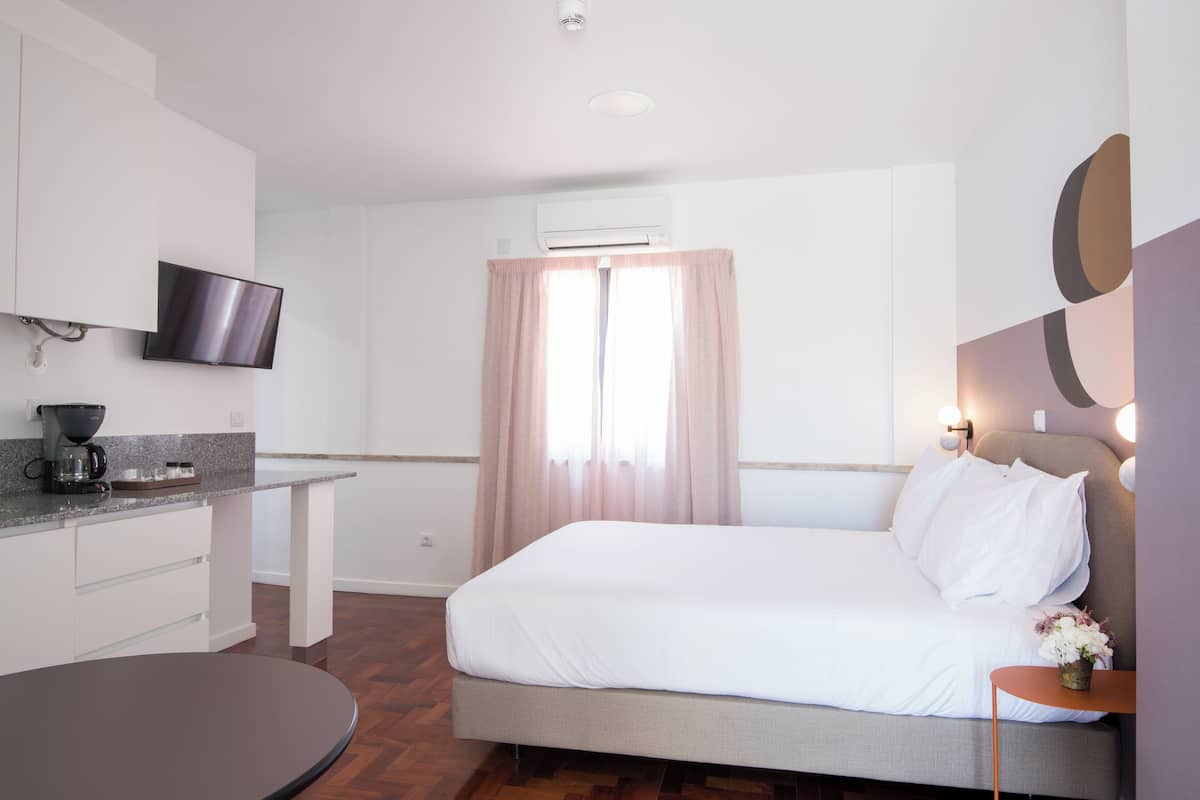 Ein modernes Hotelzimmer mit einem Bett, einem an der Wand befestigten Fernseher, einer Kaffeemaschine und einem Fenster mit Vorhängen.