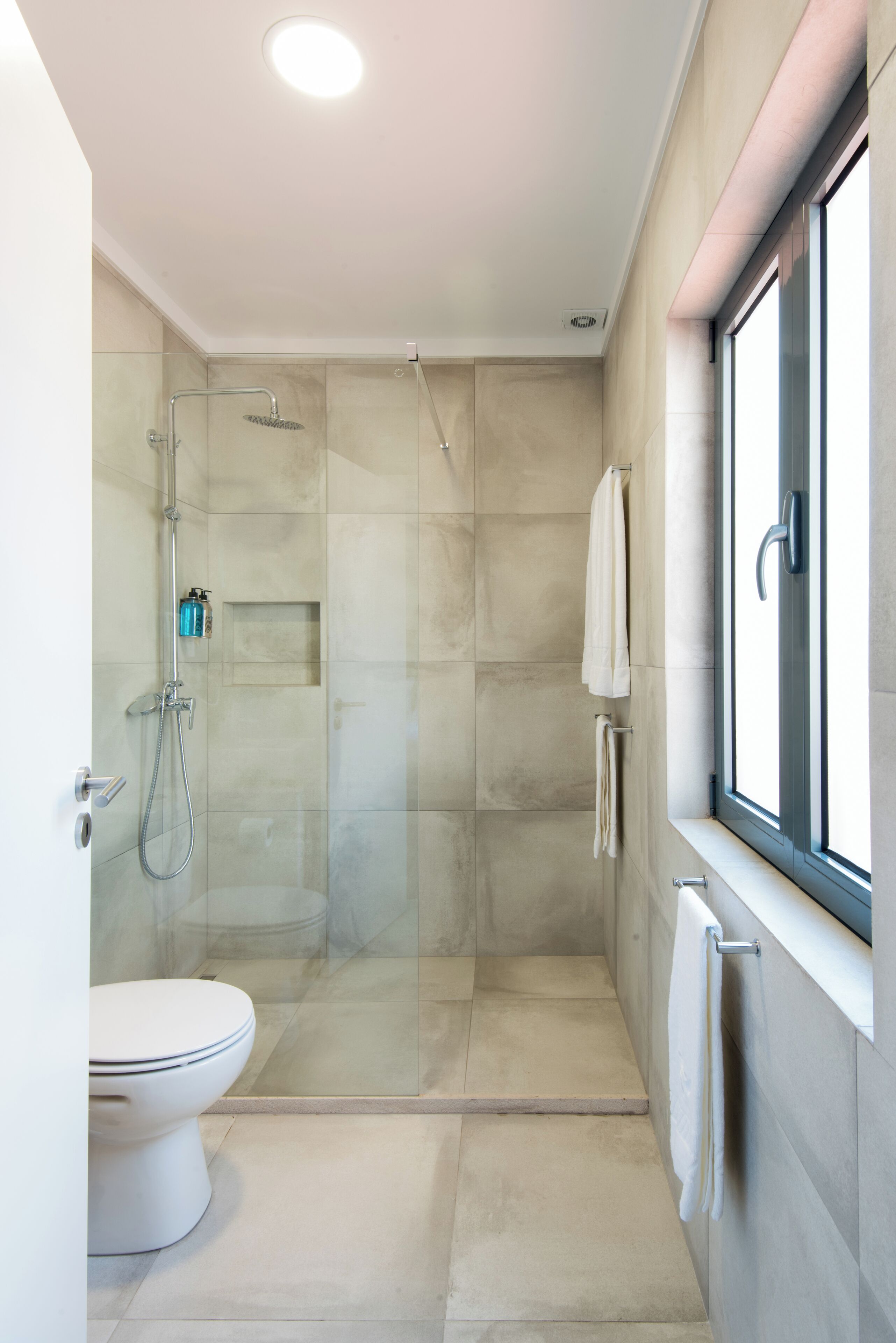 Een moderne badkamer met een douchecabine van glas, een toilet en een raam dat natuurlijk licht binnenlaat.