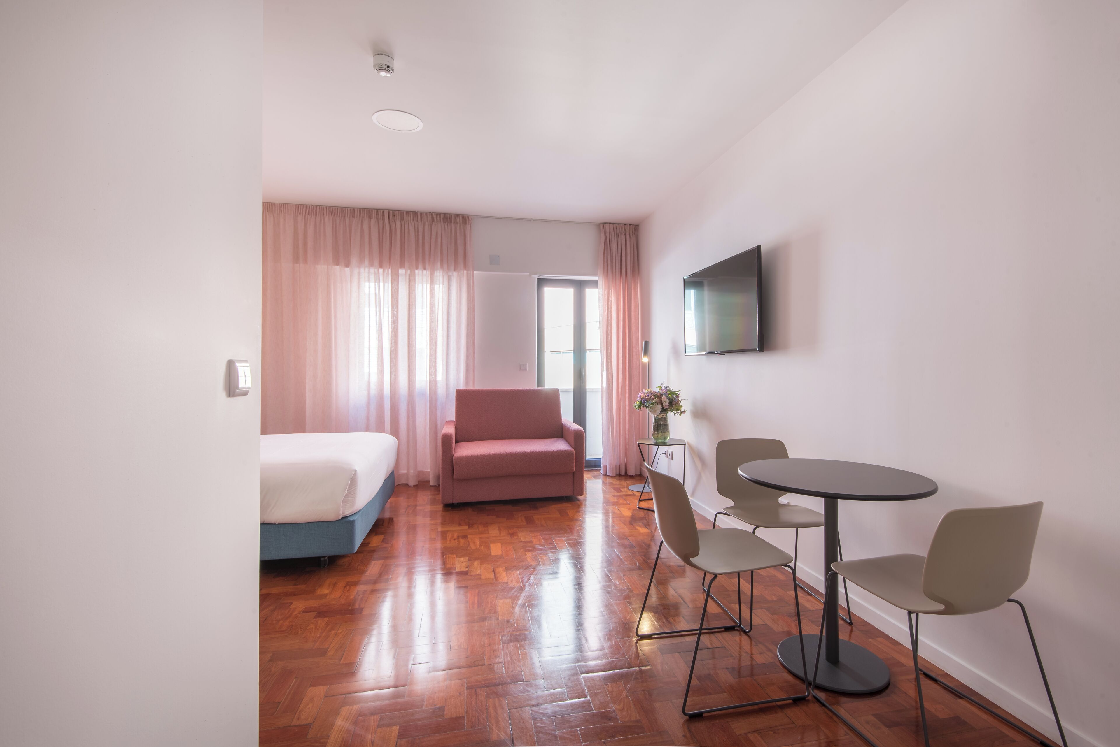 Een moderne hotelkamer met een bed, een bank, een eettafel met stoelen en een aan de muur bevestigde televisie.