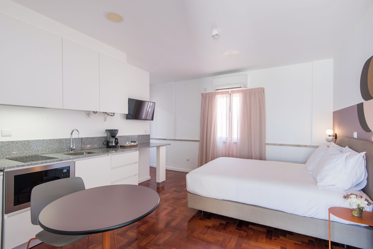 Habitación de hotel moderna con cama, una mesita, horno empotrado, televisión y ventana con cortinas.