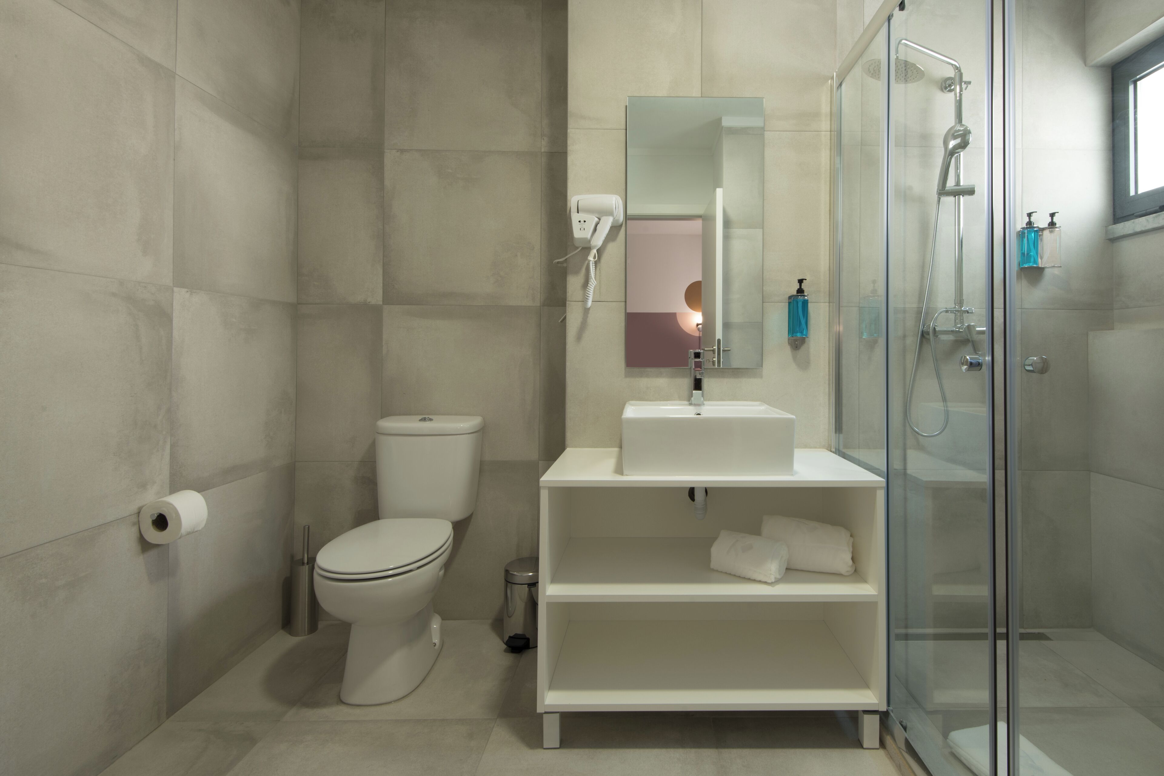 Une salle de bain moderne équipée de toilettes, d’un lavabo avec un miroir, d’une douche et d’une poubelle.