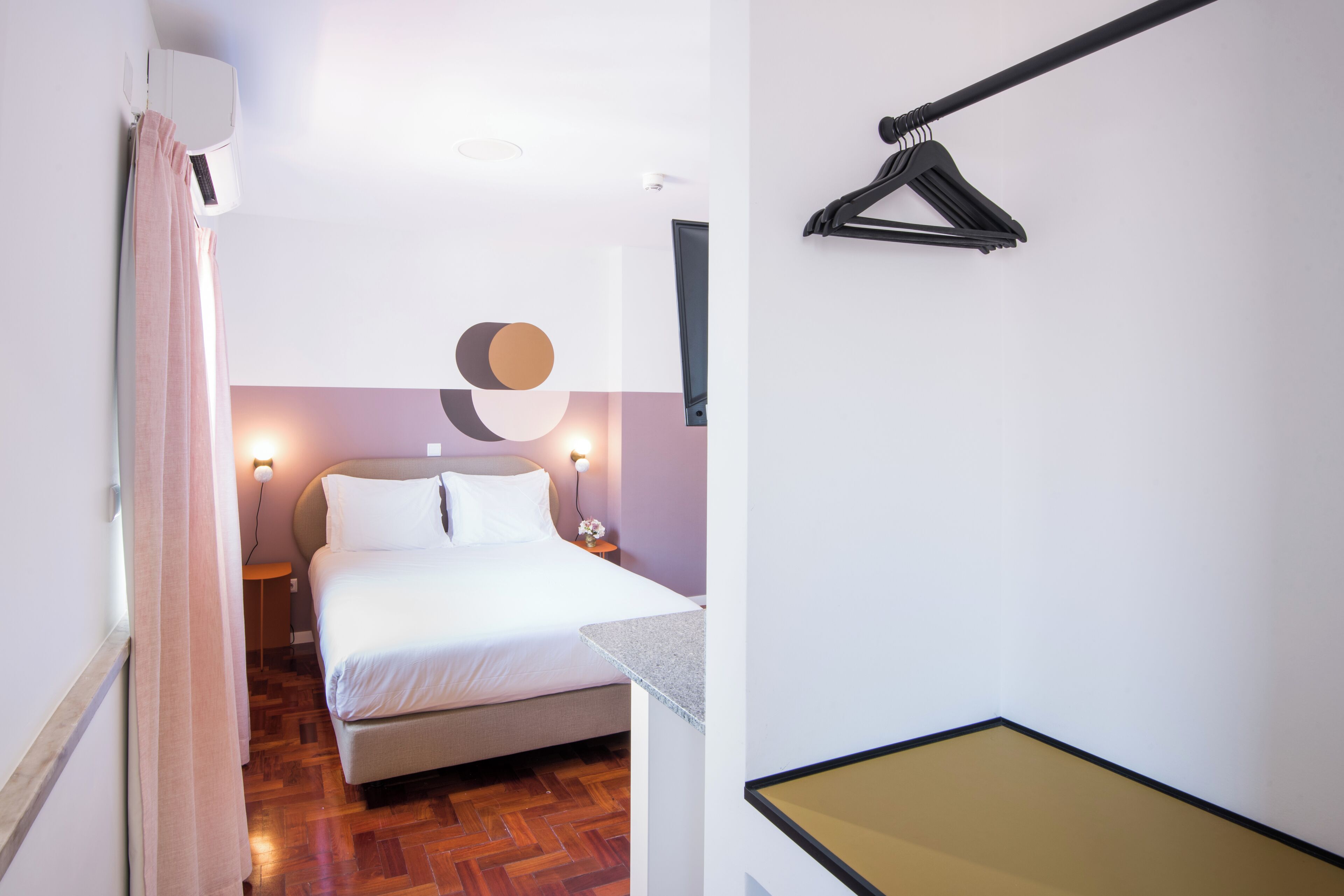 Una habitación de hotel con cama, mesita de noche, lámpara de pared y lámpara colgante.