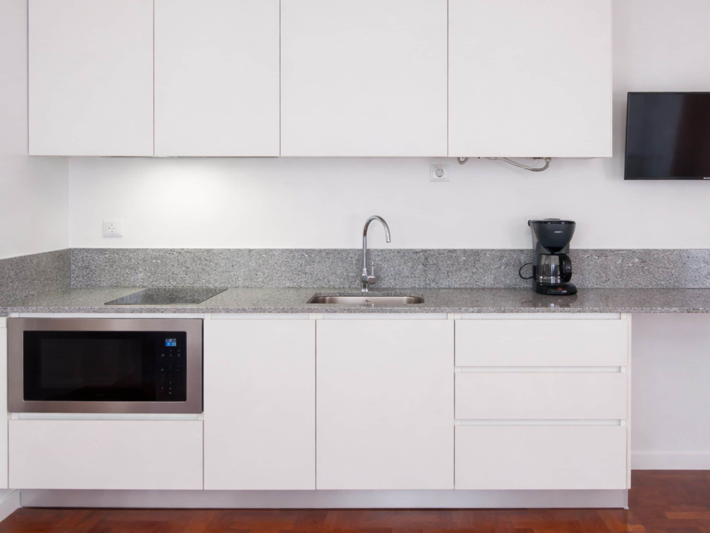 A modern kitchen with white cabinets, a stainless steel microwave, a sink, and a coffee maker.