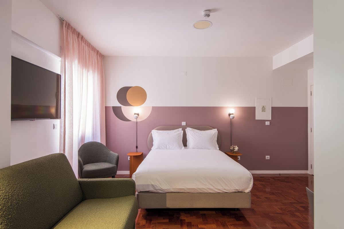 Ein Schlafzimmer mit einem Bett, einem grünen Sessel, einer runden Lampe und einem an der Wand befestigten Fernseher.