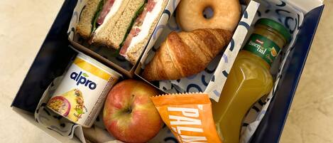 Una fiambrera con sándwiches, un croissant, una manzana, una botella de jugo, un envase de yogur y una bolsita de snack.