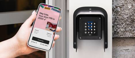 A person holding a smartphone displaying a message about a door PIN, next to a door with a numeric keypad.