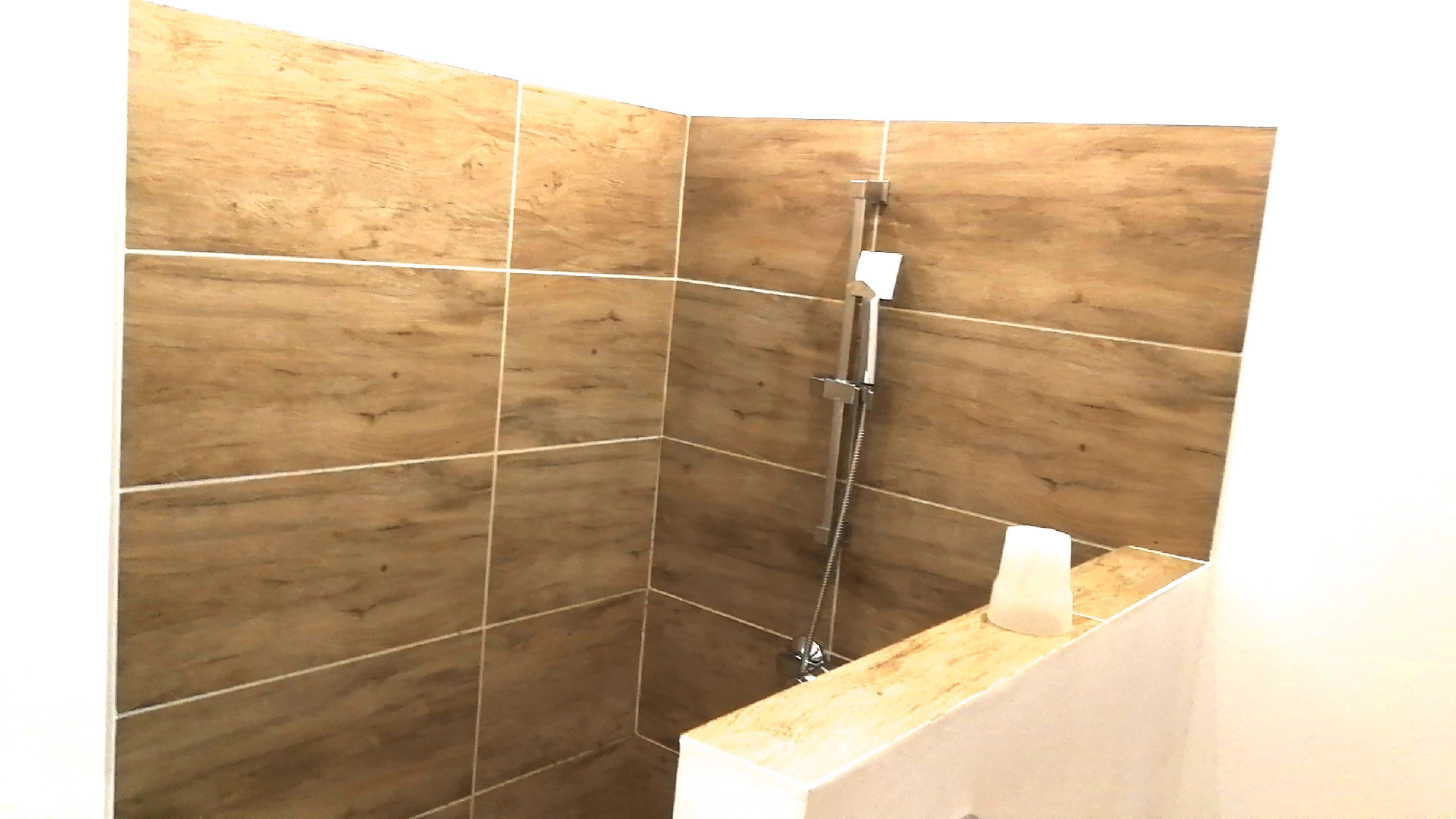 Un área de ducha con azulejos de madera y un cabezal de ducha manual.
