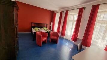 Une pièce comprenant un lit, deux chaises rouges, une table et une armoire.