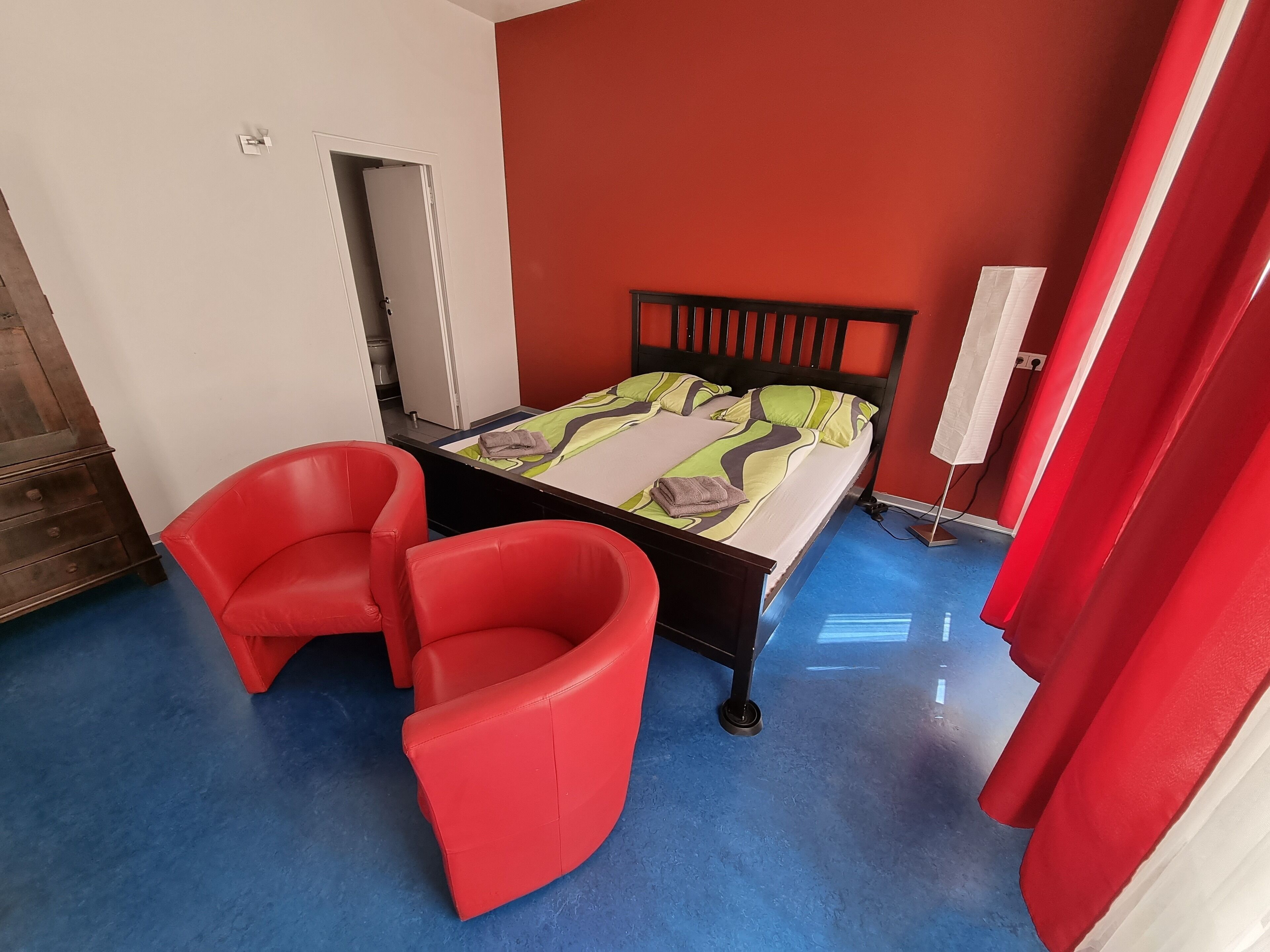 Ein Zimmer mit einem Bett, zwei roten Sesseln, einem Kleiderschrank und einem Spiegel.