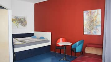 Cozy retreat with a single bed, round table, and blue chair, perfect for a relaxing stay.