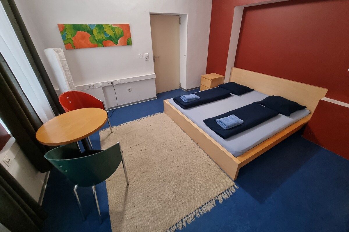A room with a bed, a desk, a chair, and a painting on the wall.