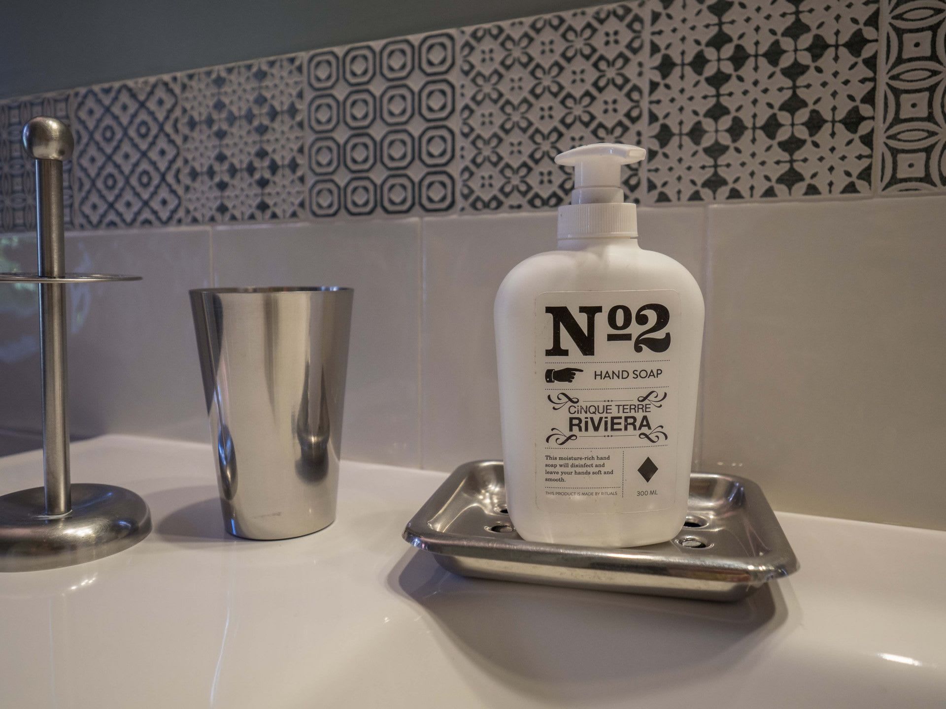 A bathroom sink with a hand soap bottle labeled 'Nº2' and a metallic cup.