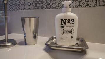 A bathroom sink with a hand soap bottle labeled 'Nº2' and a metallic cup.