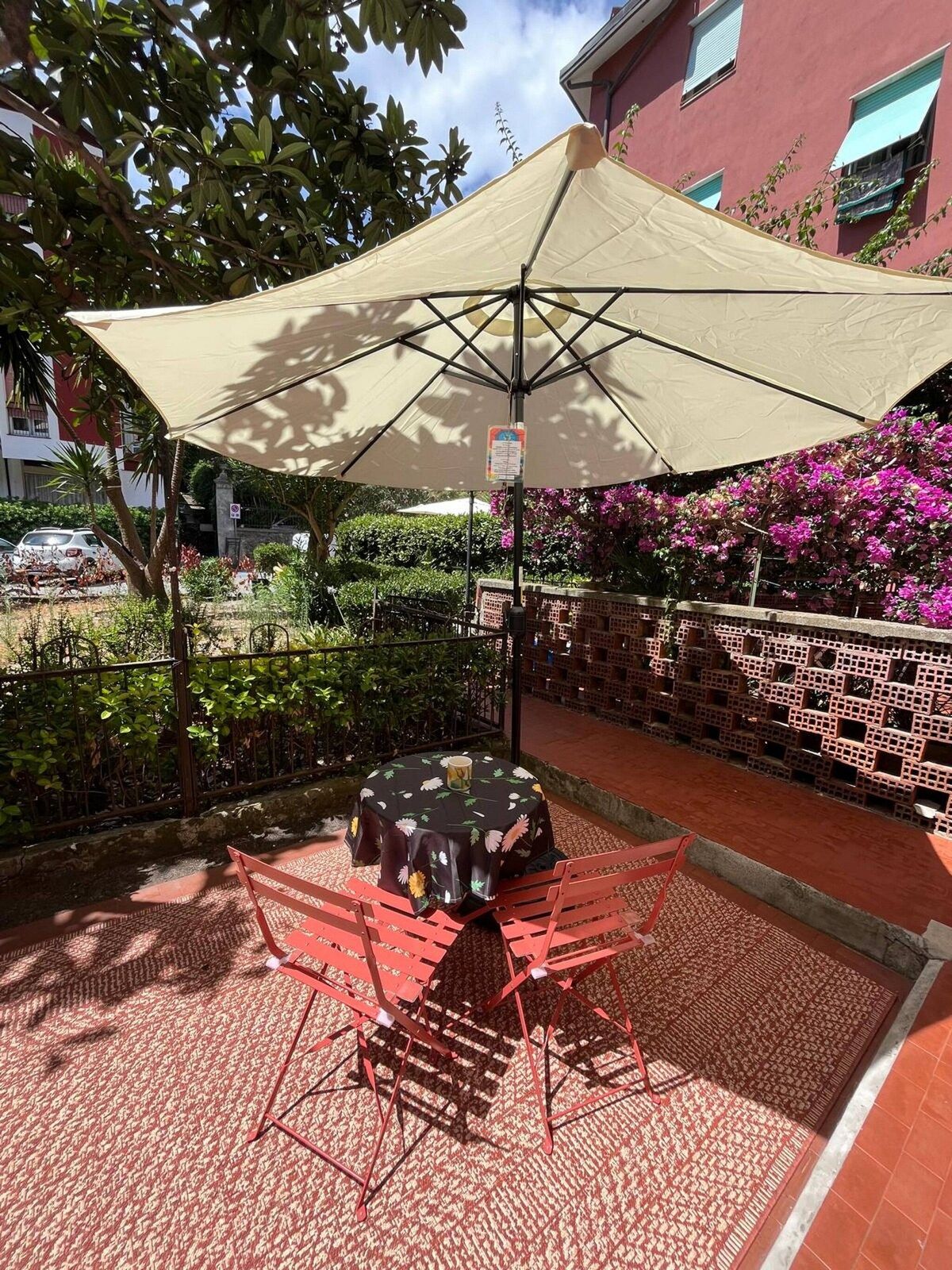Een terras met een tafel en stoelen onder een grote parasol, omringd door groen en een bakstenen muur.