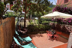 Une terrasse avec une chaise suspendue, une table avec des chaises et un parasol.
