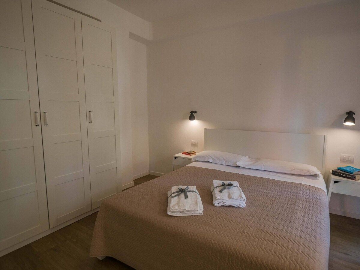 Une chambre d’hôtel comprenant un lit, deux tables de chevet, une armoire et un luminaire fixé au mur.