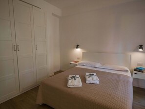 A hotel room with a bed, two nightstands, a wardrobe, and a wall-mounted light fixture. - Il Giardino di Ada Ground Floor Studio with AC and Patio (Monterosso al Mare)