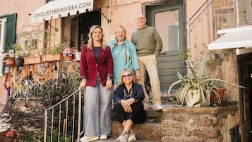 Un grup de persones demanten i assegudes a una escala de pedra davant d'un edifici amb un rètol que diu 'CINQUETERIVIERA.COM'.