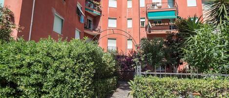 A pathway leading to a multi-story building with balconies, surrounded by greenery and a bicycle.