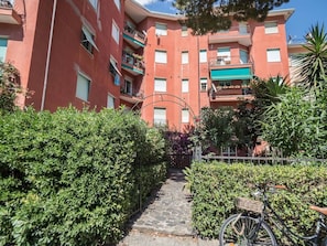 Un chemin menant à un immeuble à plusieurs étages doté de balcons, entouré de verdure et avec un vélo à proximité.