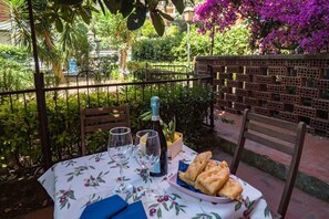 An outdoor dining area with a table set for two, featuring a bottle of wine, glasses, and a plate of bread.