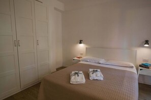 A bedroom with a bed, two towels, a nightstand, a lamp, and a wardrobe.