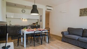 A modern kitchen with white cabinets, a dining table with chairs, and a grey sofa. - Scimiscià 2 bedroom Apartment (Monterosso al Mare)