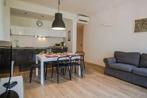 A modern kitchen with white cabinets, a dining table with chairs, and a grey sofa.