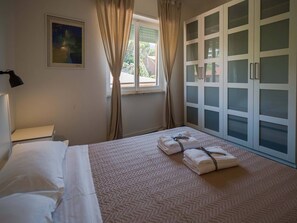 A hotel room with a bed, a nightstand, a window with curtains, a painting on the wall, and a wardrobe with frosted glass doors.