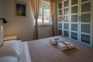Een slaapkamer met een bed, een raam met gordijnen, een wandlamp en een deur met geëtste glaspanelen.