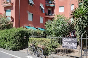 A red building with balconies, a bicycle, and a sign for 'LA FENICE IMMOBILIARE VENTE'.