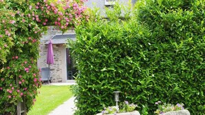 A garden pathway leading to a stone building with a purple umbrella.