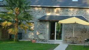 A stone building with a covered patio, a palm tree, and a gravel path leading to the entrance.
