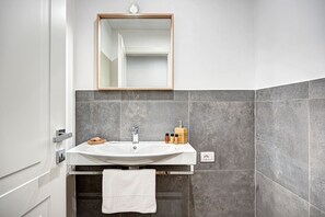 Ein Badezimmer mit Waschbecken, Spiegel und grauen Fliesen.